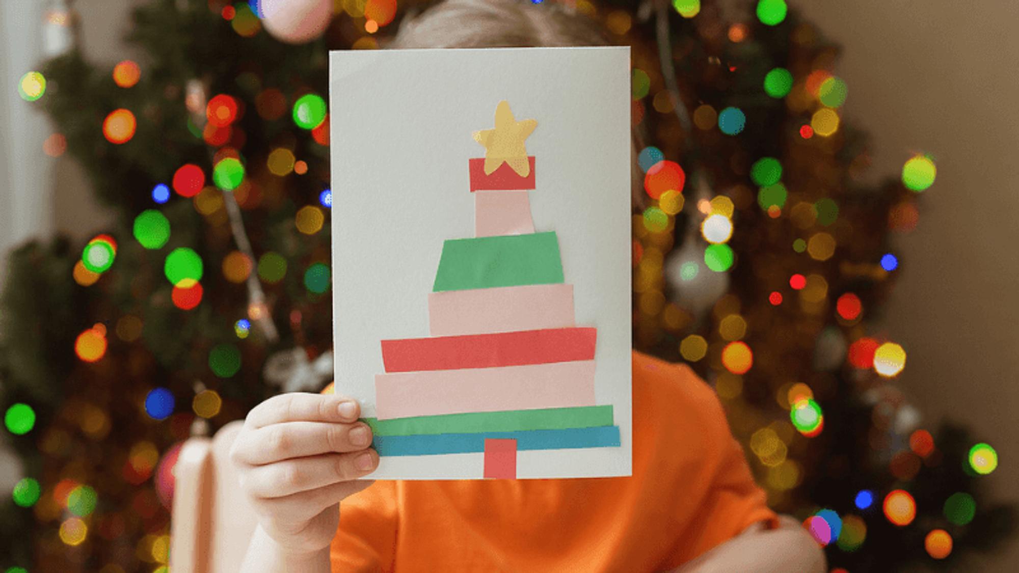 Kind hat Weihnachtskarte gebastelt mit Tannenbaum-Motiv
