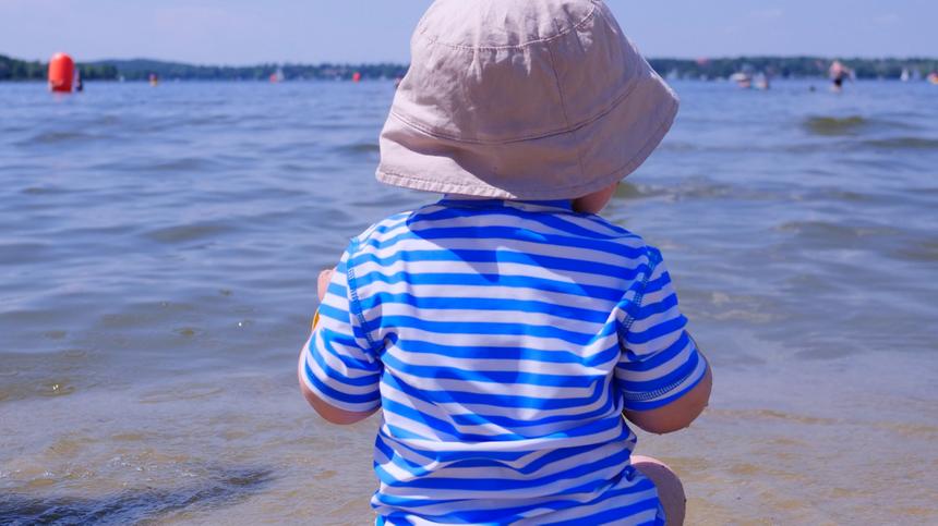 Sonnenschutz: Baby sitzt mit UV-Kleidung am Wasser