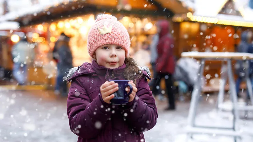 Kleines Mädchen pustet auf einem Weihnachtsmarkt in eine Tasse