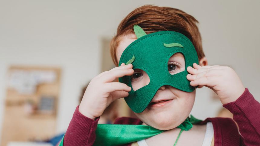 Verkleidungskiste: Kind hält eine grüne Maske vors Gesicht