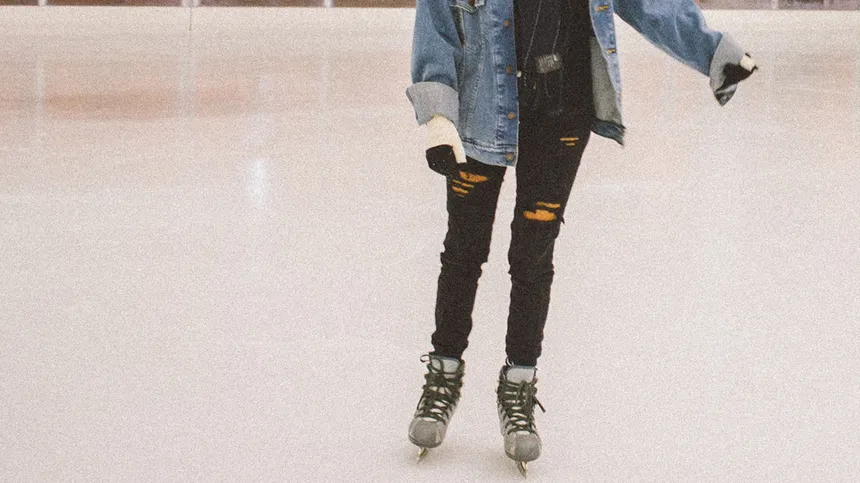 Mädchen in Jeansjacke läuft mit Schlittschuhen über das Eis