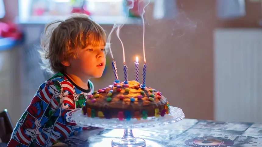 Kind pustet Kerzen auf Kuchen aus