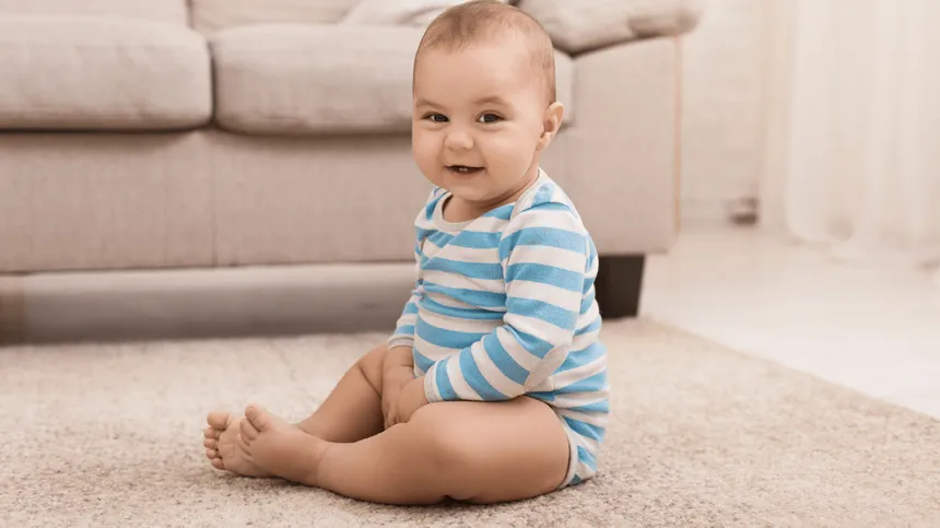 Ein 12 Monate altes Baby in gestreiftem Body sitzt auf dem Boden