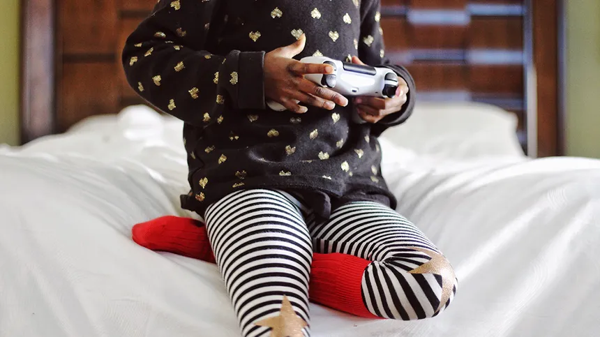Ein Mädchen sitzt auf eine Bettkante und spielt Videospiele