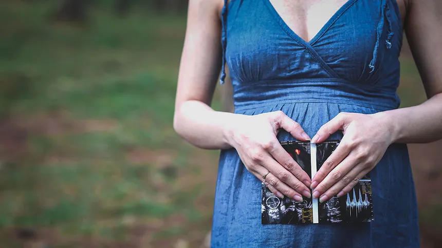 Schwangere Frau hält Ultraschallbild vor ihren Babybauch