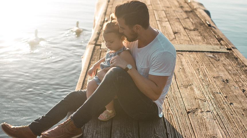 Vater und Tochter sind gemeinsam am See und sehen den Enten zu