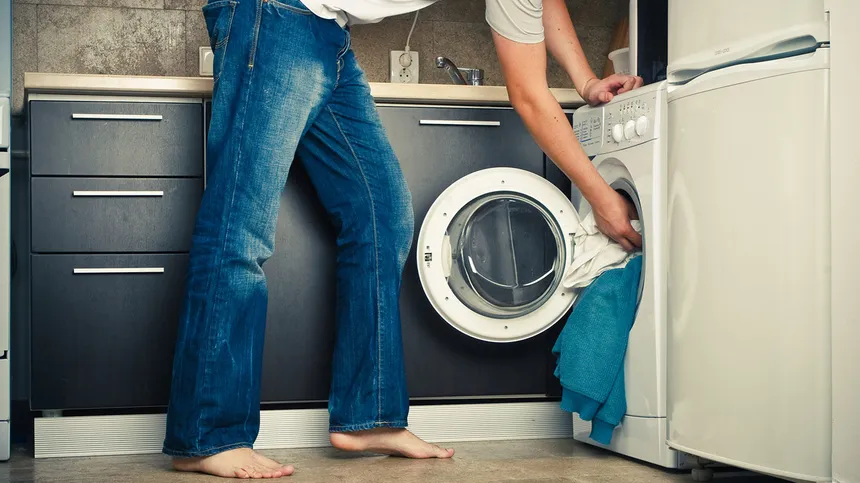 Mann steck Wäsche in die Waschmaschine