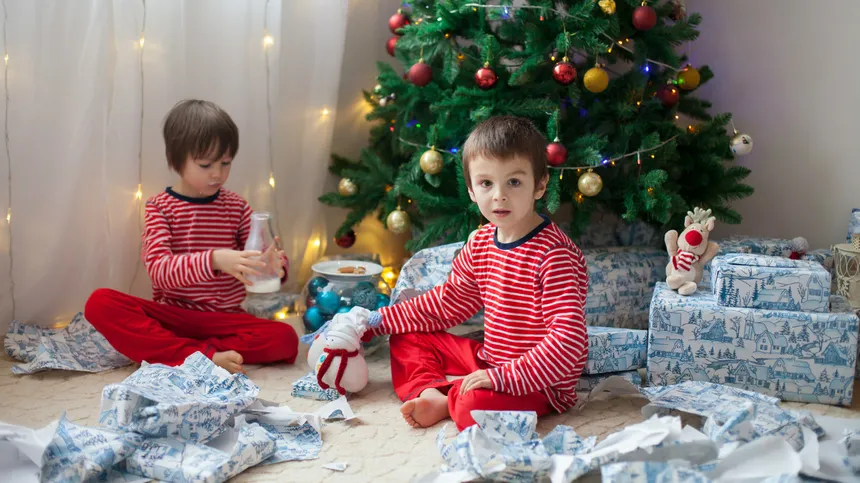 Zwei Kinder sitzen mit ihren Geschenken unter dem Weihnachtsbaum.