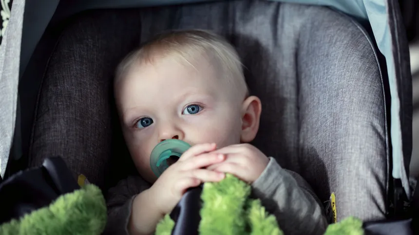 Ein kleiner Junge sitzt mit seinem Schnuller im Mund im Kindersitz