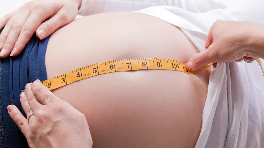 Eine schwangere Frau hat ein Maßband auf dem Bauch