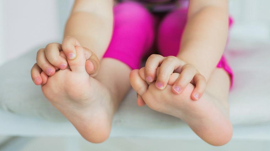 Ein Kleinkind fasst mit den Händen an seine Füße.