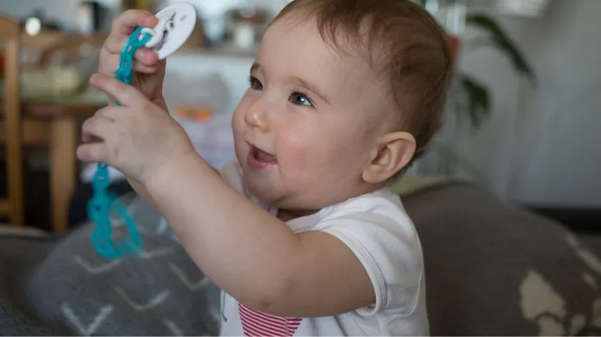 Baby mit DIY-Schnullerkette in den Händen