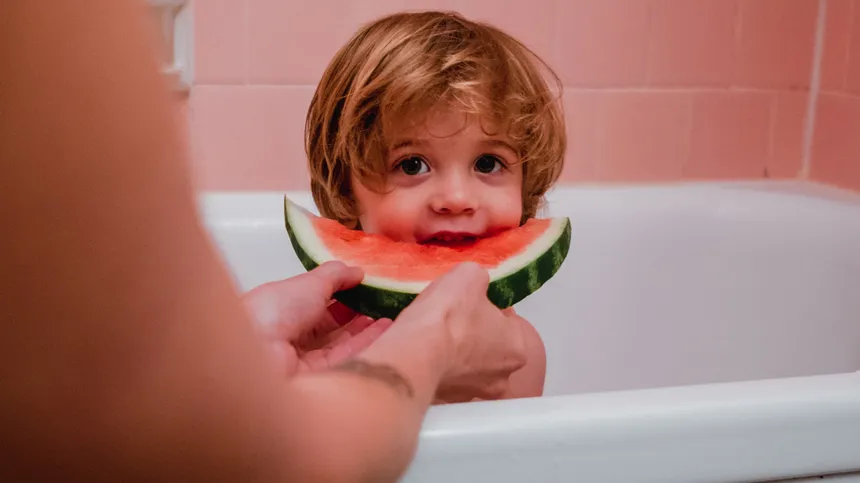 Kind sitzt in einer Badewanne und isst eine Melone