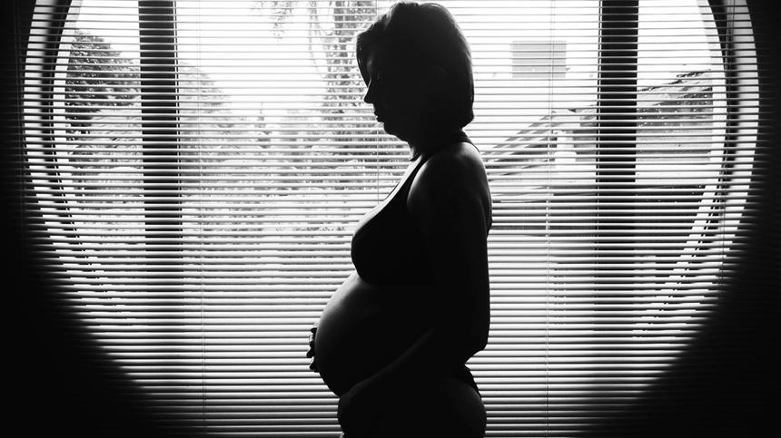 Schwangere Frau steht vor einem Fenster in schwarz weiß