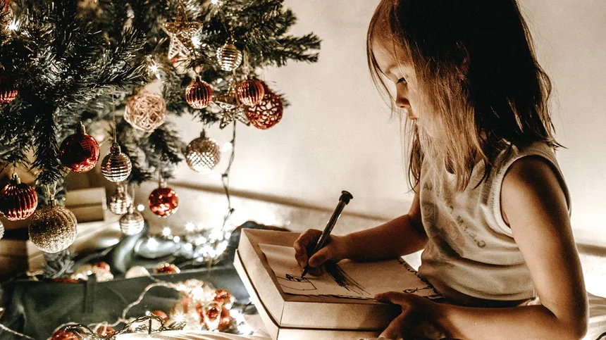 Mädchen schreibt Wunschzettel vor Christbaum