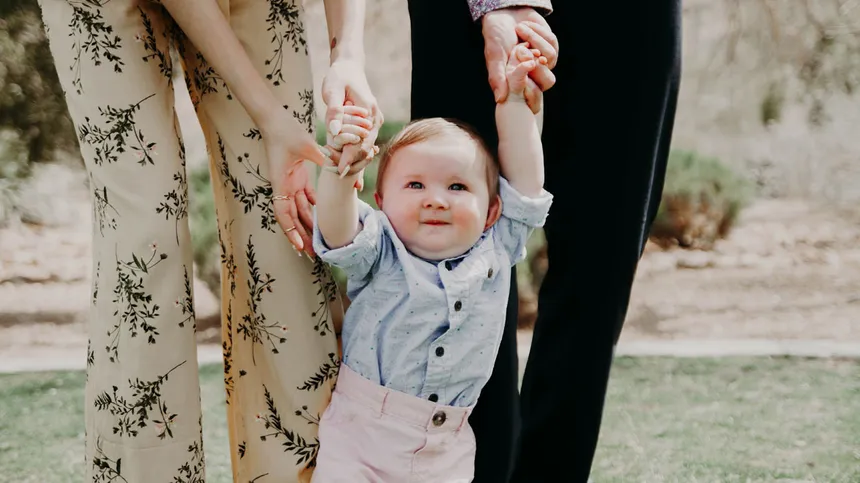 Baby läuft an den Händen seiner Eltern