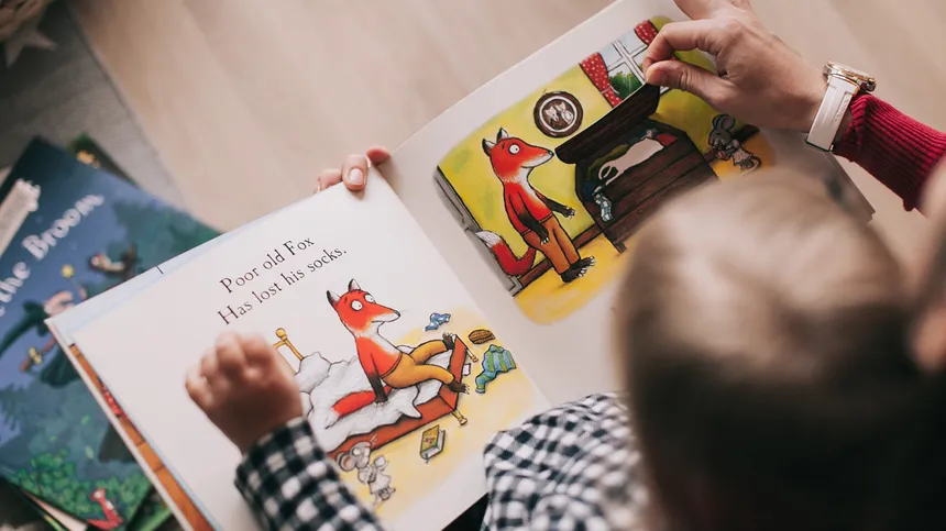 Kind liest ein Buch mit einem Erwachsenen