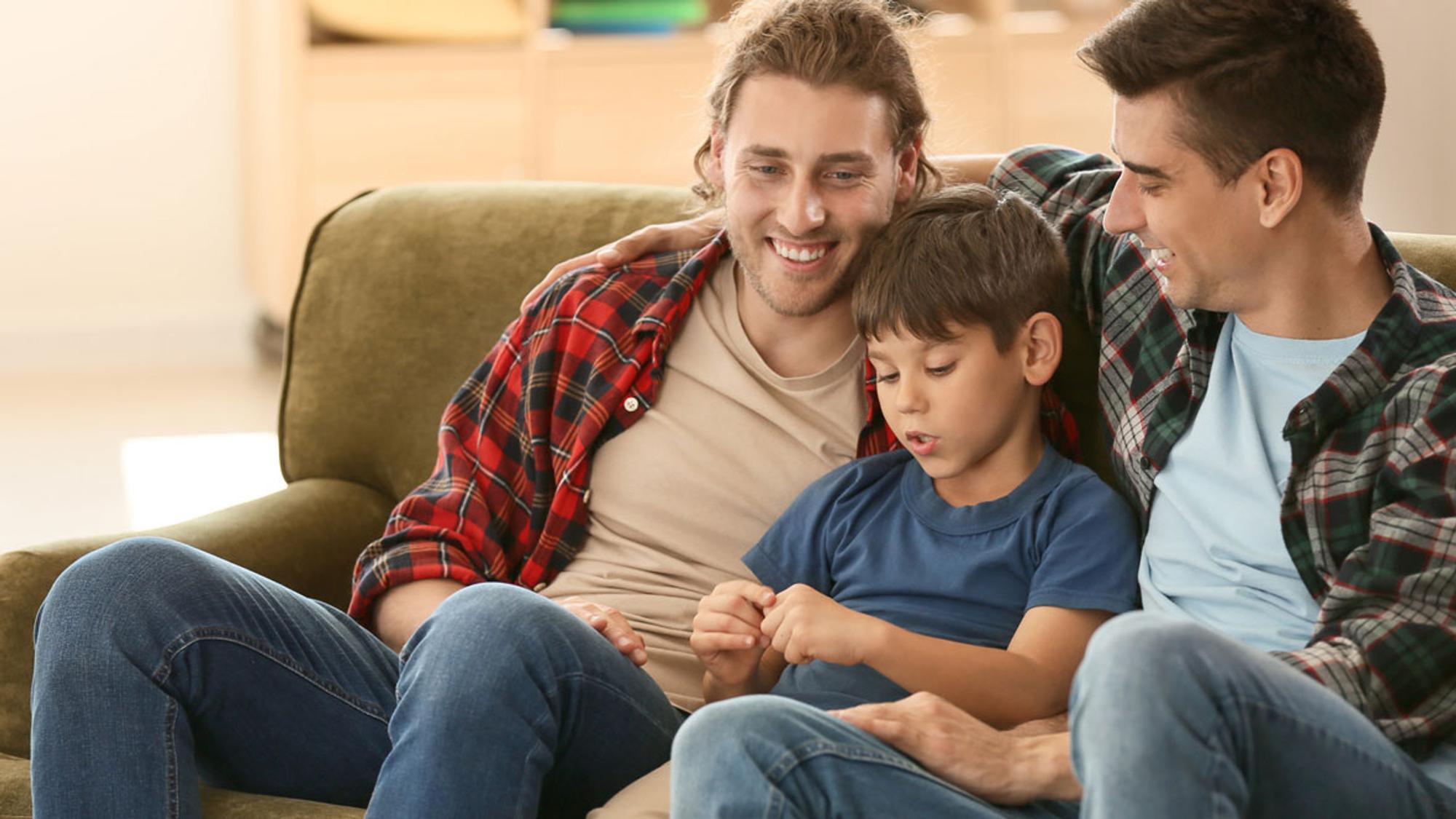 Regenbogenfamilie: Zwei Männer sitzen mit ihrem Sohn auf dem Sofa