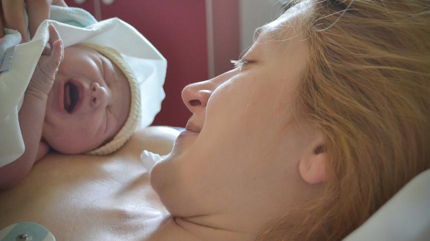 Mutter liegt im Krankenhausbett und hält ihr Neugeborenes im Arm