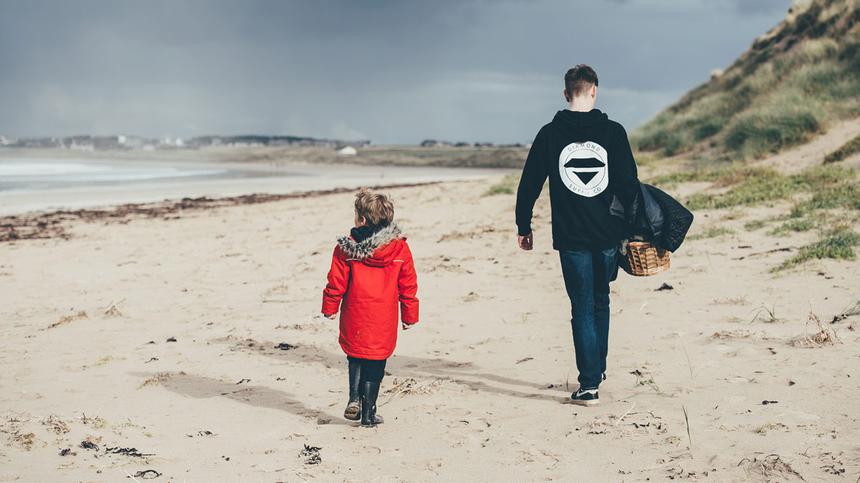 Zwei Kinder gehen hintereinander am Strand entlang