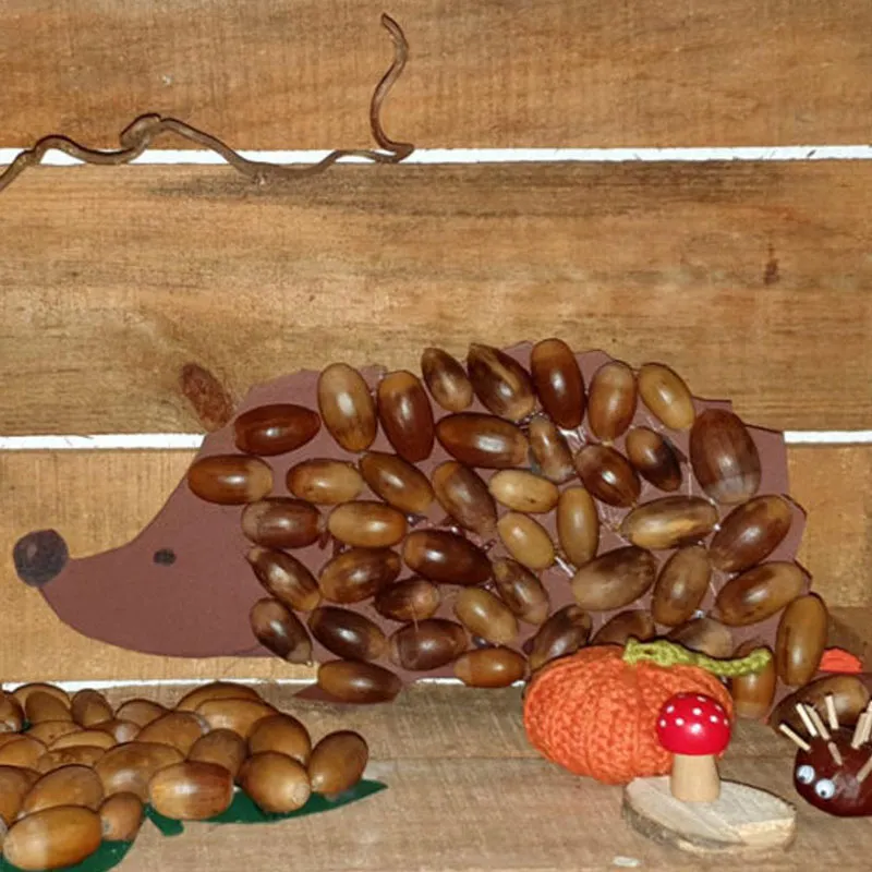 Igel mit Eicheln gebastelt, vor einer Holzwand