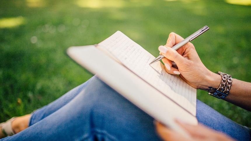 Frau sitzt im Gras und schreibt in ein Buch