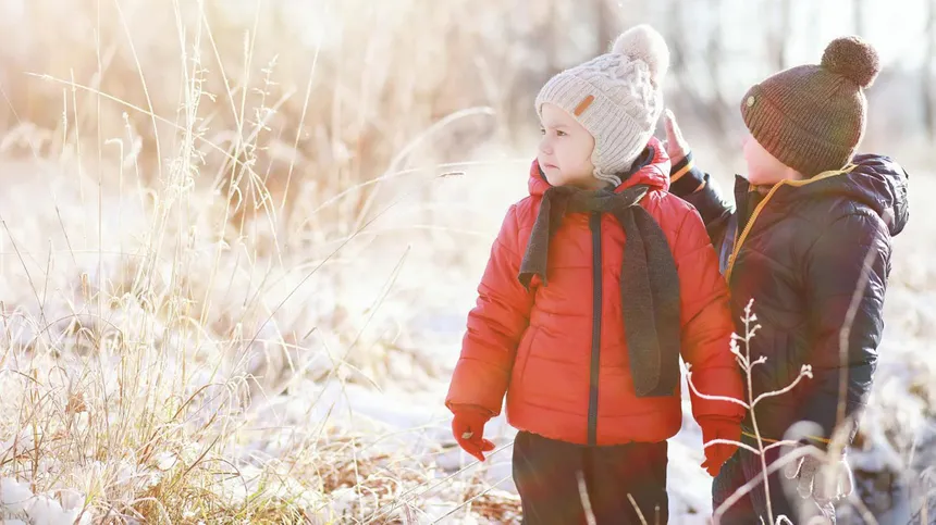 Zwei Kinder in Daunenjacken gehen im Winter spazieren