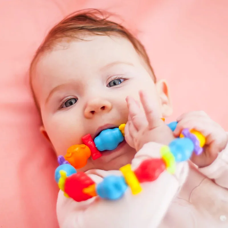 Baby liegt auf rosa Decke mit Spielzeug im Mund