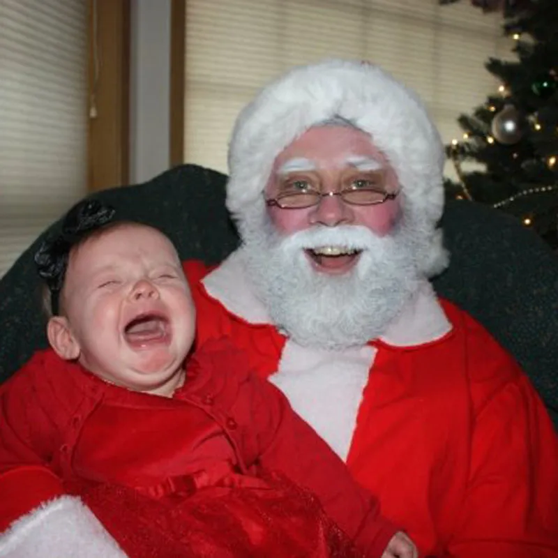 Weinendes Baby-Mädchen im roten Kleid auf dem Arm des Weihnachtsmanns