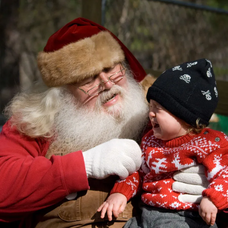 Baby mit Strickpulli und schwarzer Mütze weint wegen Weihnachtsmann
