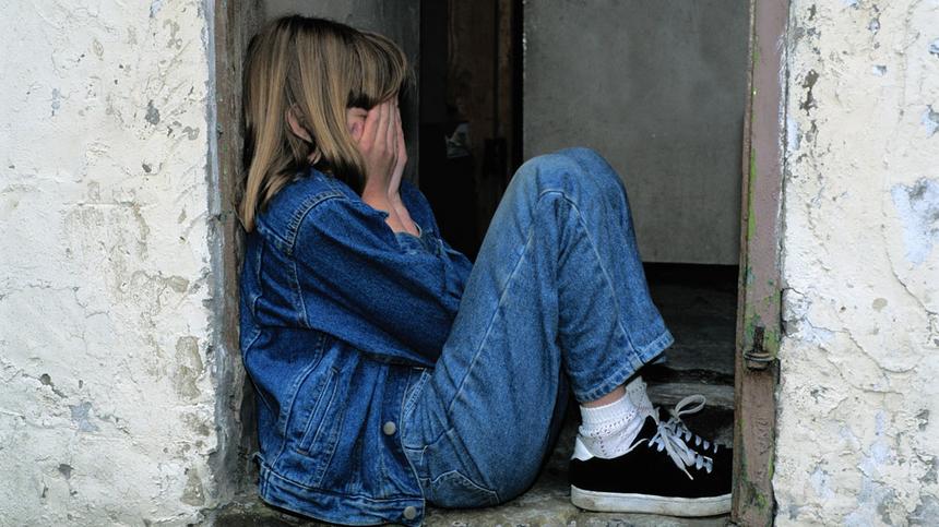 Trauriges Mädchen sitzt an einem Türrahmen