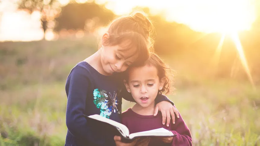 Zwei Mädchen stehen in einem Feld und lesen ein Buch