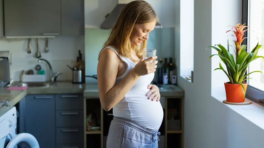 Schwangere steht in der Küche und trinkt Leitungswasser