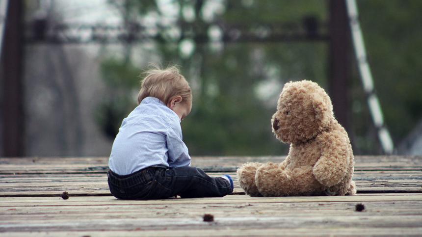 Kind und Teddy sitzen traurig da