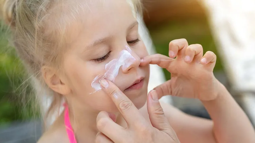 Kind trägt Sonnencreme auf die Nase auf