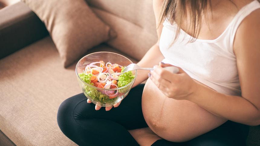 Schwangere isst auf der Coch einen Salat