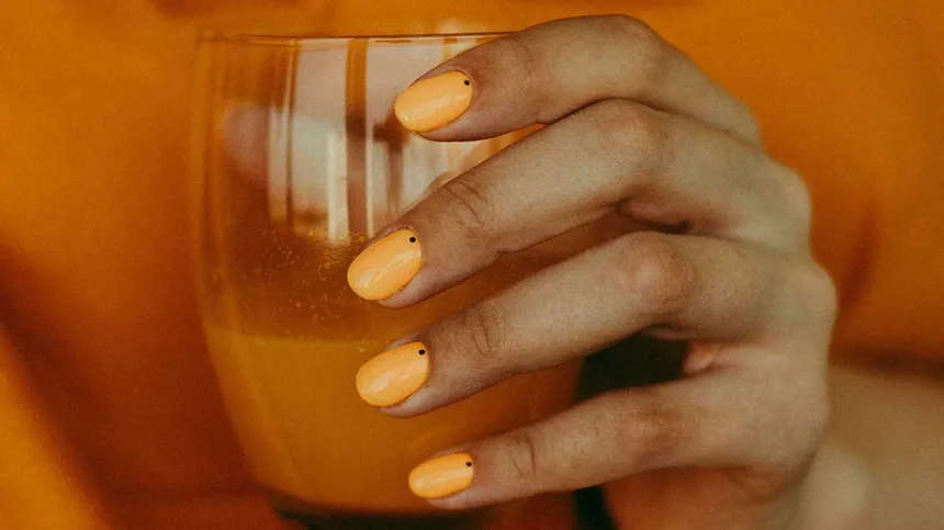 Frau mit orangenem Nagellack hält Glas