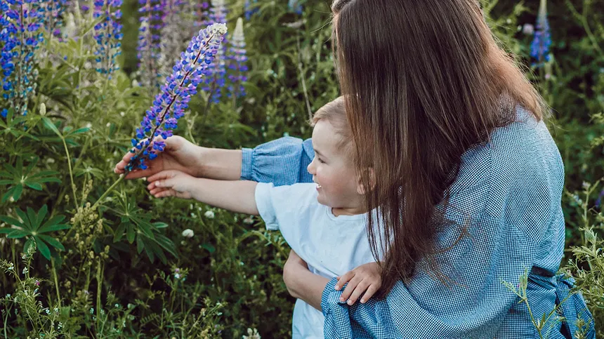 Mama pflückt mit Baby eine lila Blume