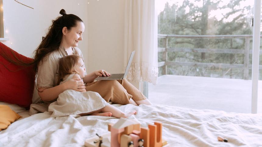 Frau mit Kind und Laptop im Bett