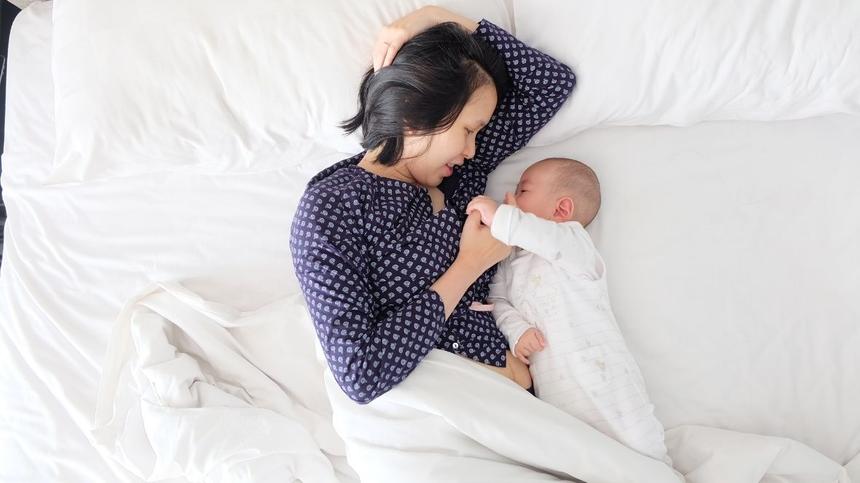 Frau liegt mit Baby im Bett