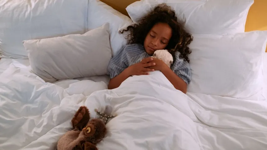 Mädchen schläft mit Kuscheltieren im Bett