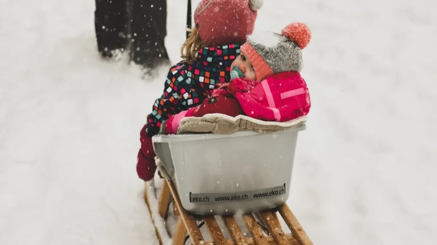 Baby in Winterkleidung wird auf Schlitten gezogen