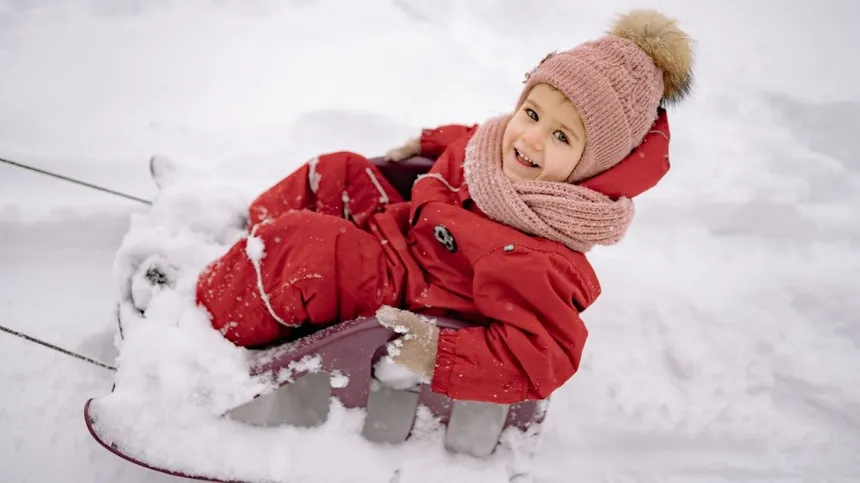 Kleines Kind sitzt auf Schlitten im Schnee