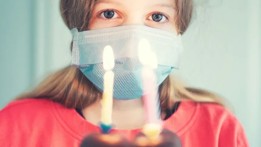 Mädchen mit Maske hält Geburtstagskerzen vor sich