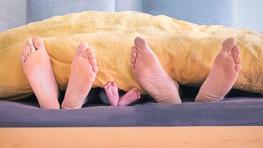 Zwei große und ein kleines nacktes Fußpaar unter Bettdecke
