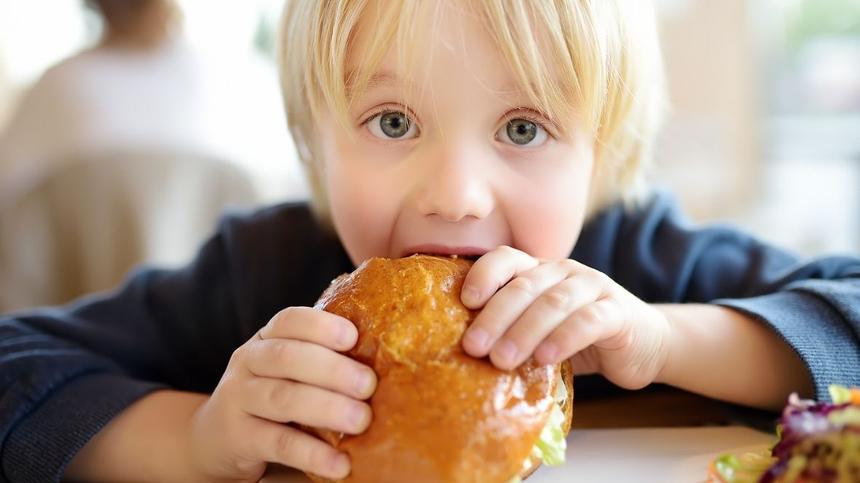 Kleiner blonder Junge isst Burger