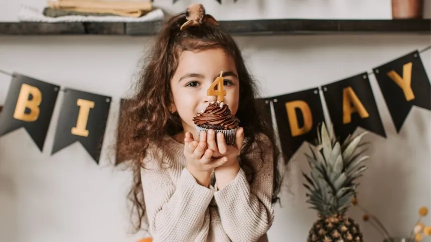 Mädchen hält dekorierten Muffin mit Kerze in Zahlenform Vier hoch