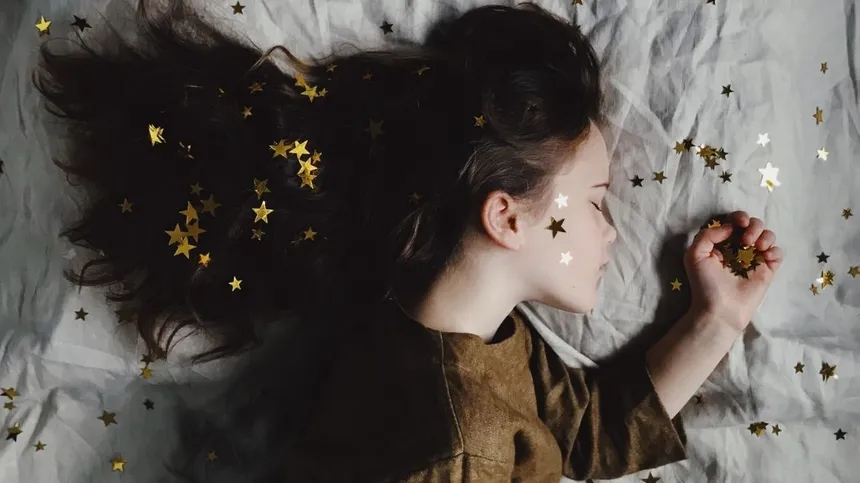 Mädchen liegt auf Bett mit Sternen im Haar und der Hand