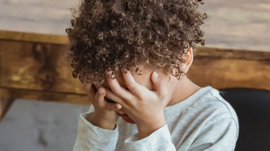 Ein Kind mit Migräne hält sich die Hände vors Gesicht
