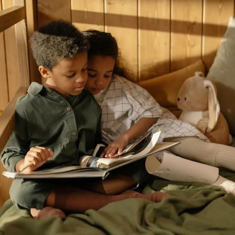 Zwei Kinder machen es sich zum Lesen gemütlich im Bett